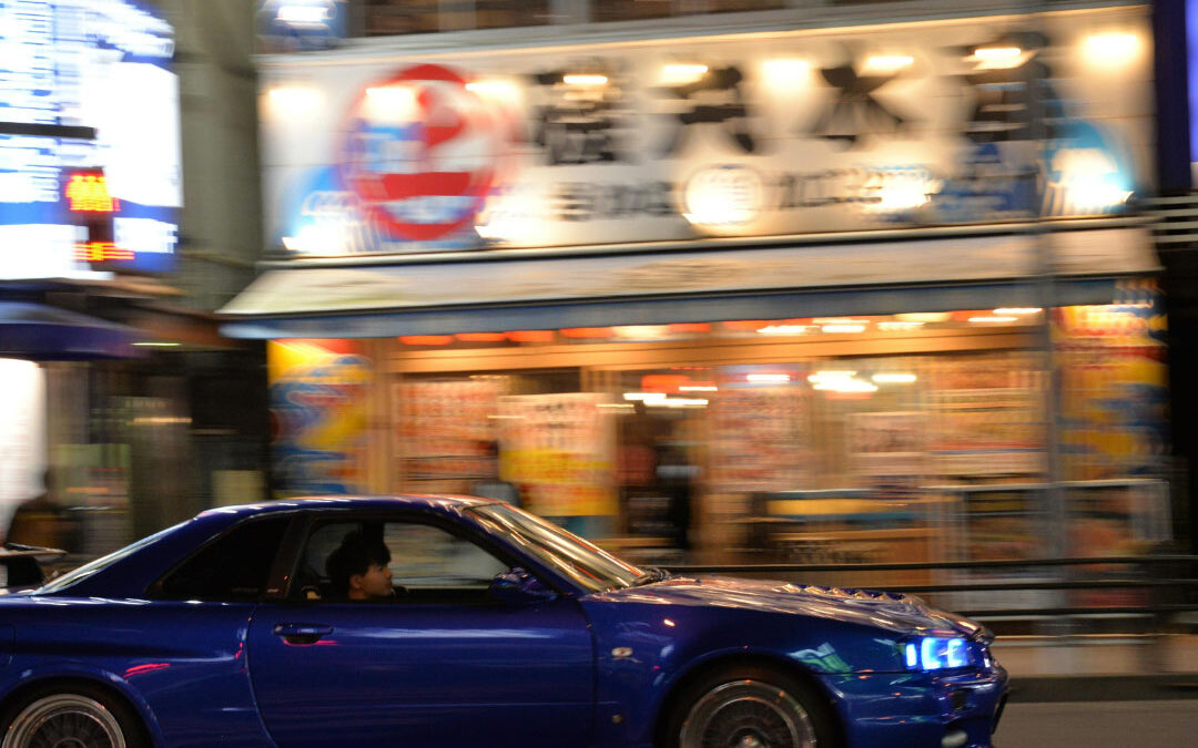 Blue sports car driving fast on a city street - www.quarantelloinsurance.com