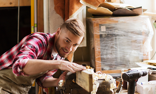 A man focused on shaping a piece of wood with tools in a workshop setting